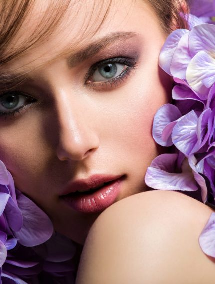 Pretty woman with bright makeup. Beautiful white girl with purpl Pretty woman with bright makeup. Beautiful white girl with purple flowers. Stunning brunette girl with big bouquet of hydrangeas. Closeup face of young beautiful woman with a healthy clean skin.